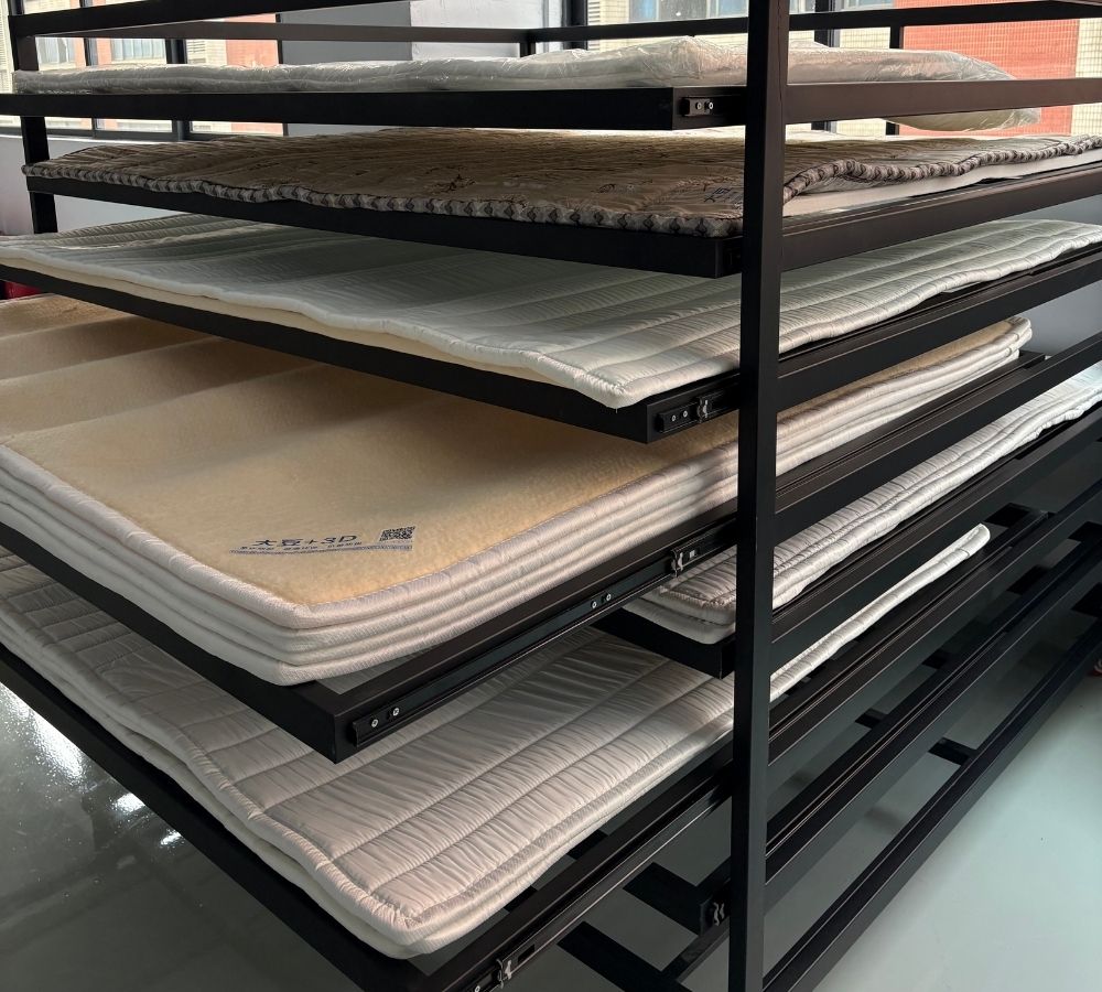 A black metal mattress rack holding multiple stacked mattress or mattress-toy samples, photographed indoors on a glossy floor.