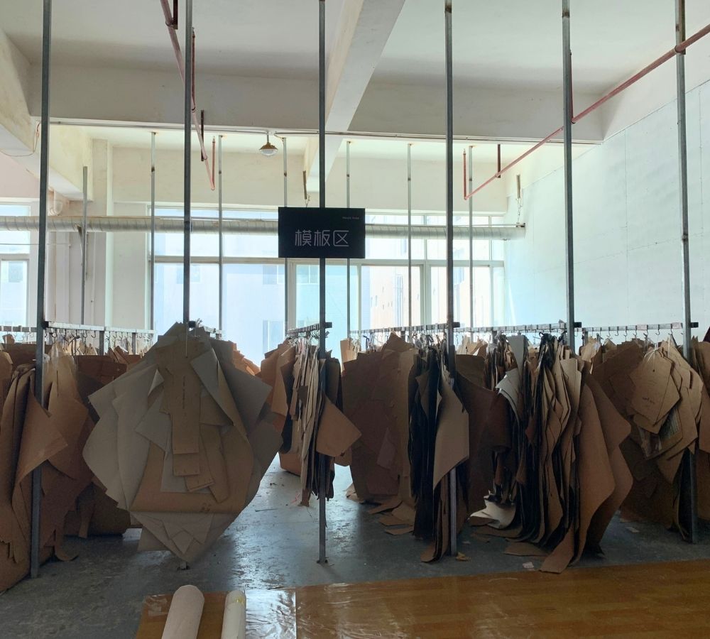 A large indoor production space with many hanging sofa moulds on metal racks, including several large irregular brown paper/cardboard-like fabric forms. A black sign hangs in the center with Chinese text.