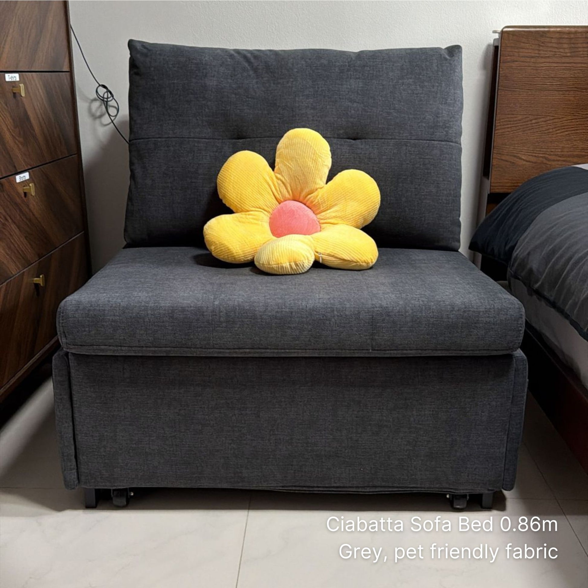 Gray sofa bed with a yellow flower-shaped pillow in a room setting.