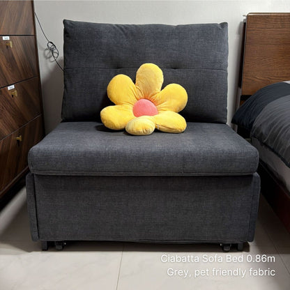 Gray sofa bed with a yellow flower-shaped pillow in a room setting.
