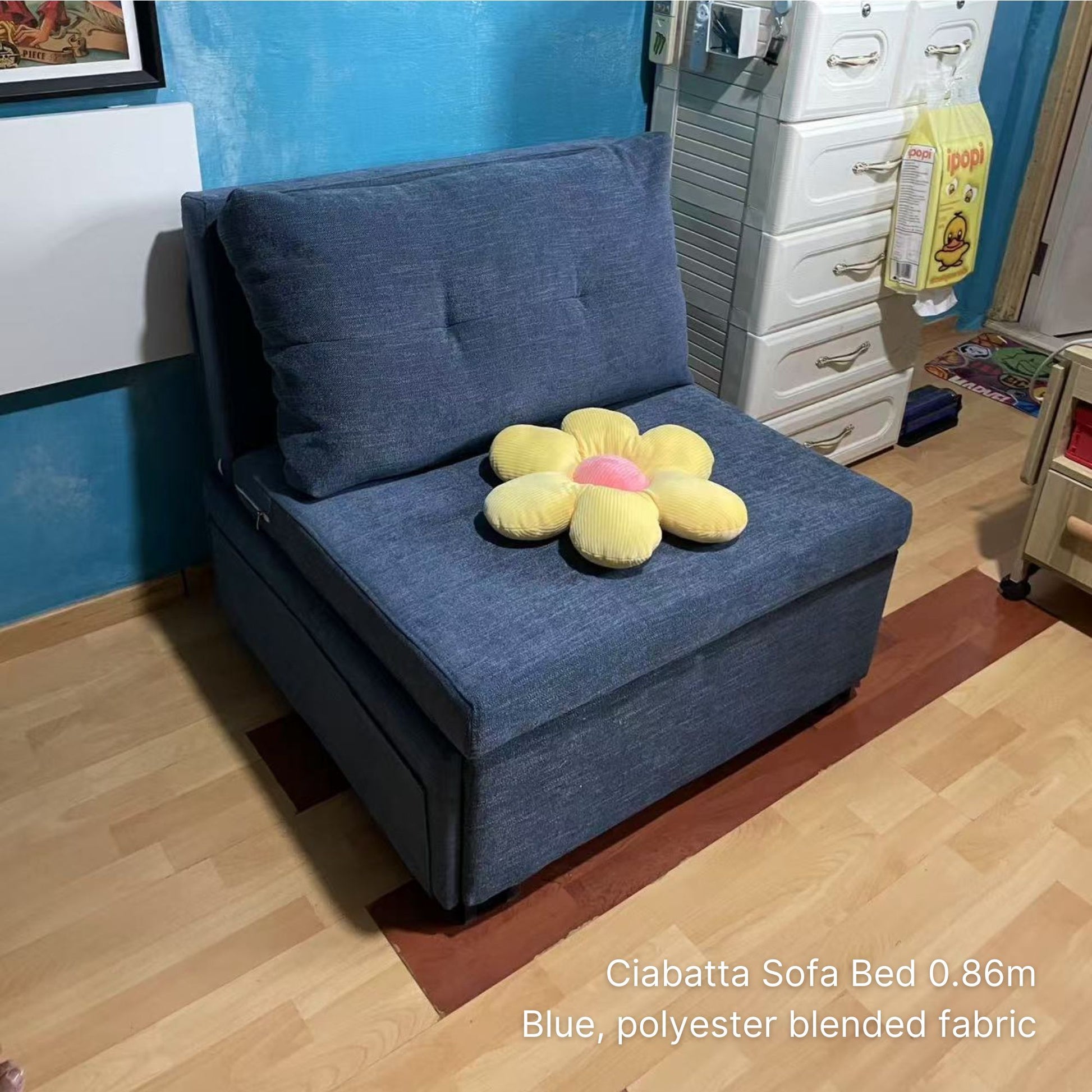 Blue sofa bed with a yellow flower-shaped pillow in a room setting.