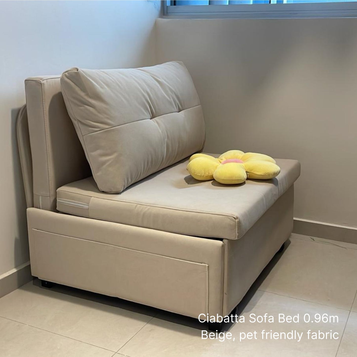 Beige sofa bed with a pillow and plush toys in a room.