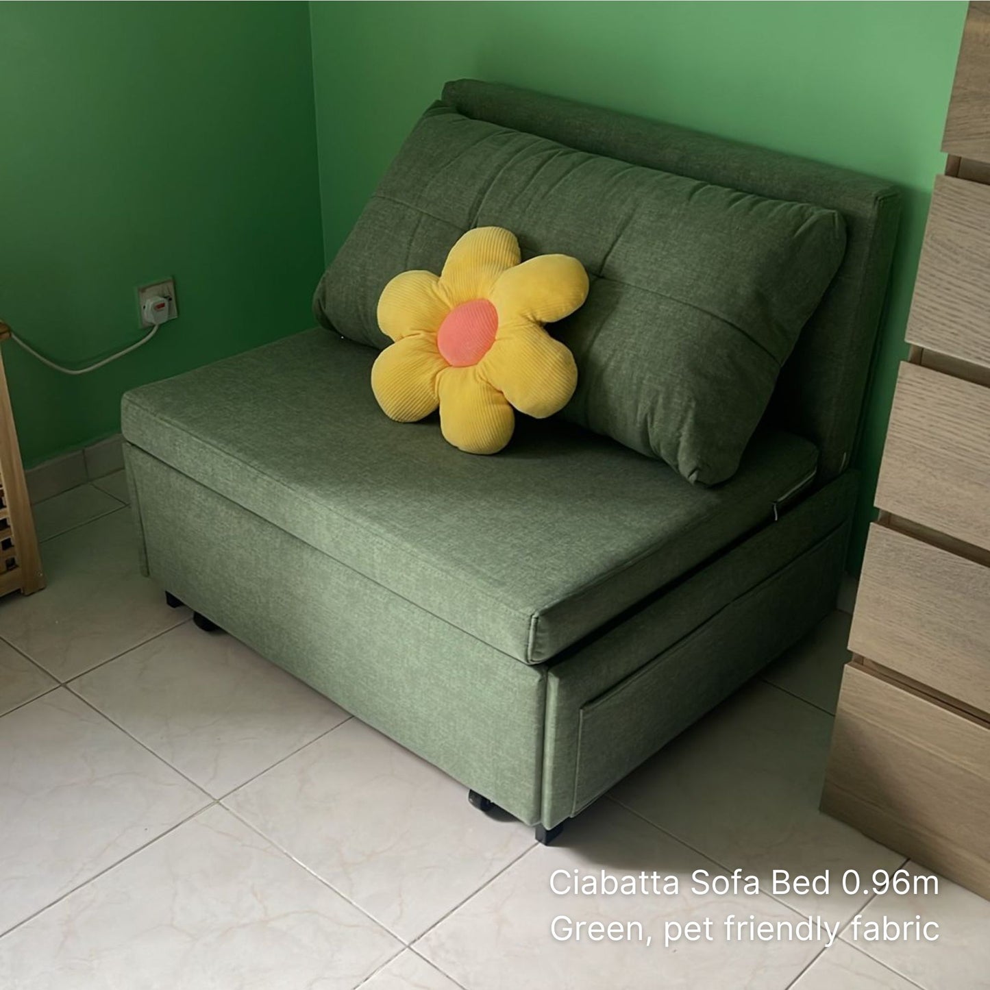 Green sofa bed with a yellow flower pillow against a green wall.