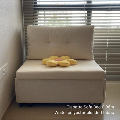 White sofa bed with a yellow flower-shaped pillow in a room with window blinds.