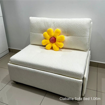White sofa bed with a yellow flower-shaped pillow on a tiled floor.