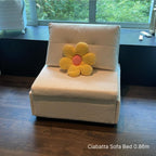 White sofa bed with a yellow flower-shaped pillow in a room with a window and desk.