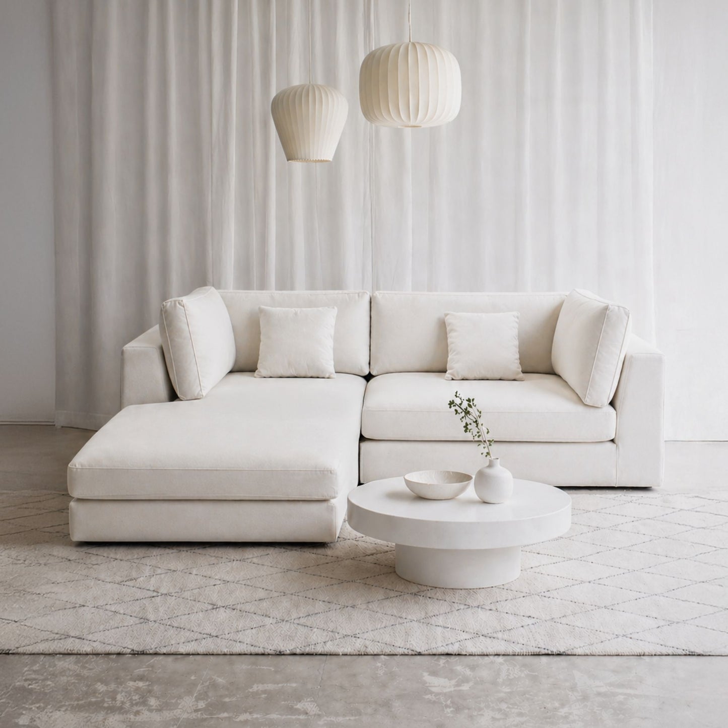 Modern white sectional sofa in a minimalistic living room with a coffee table and decorative items.