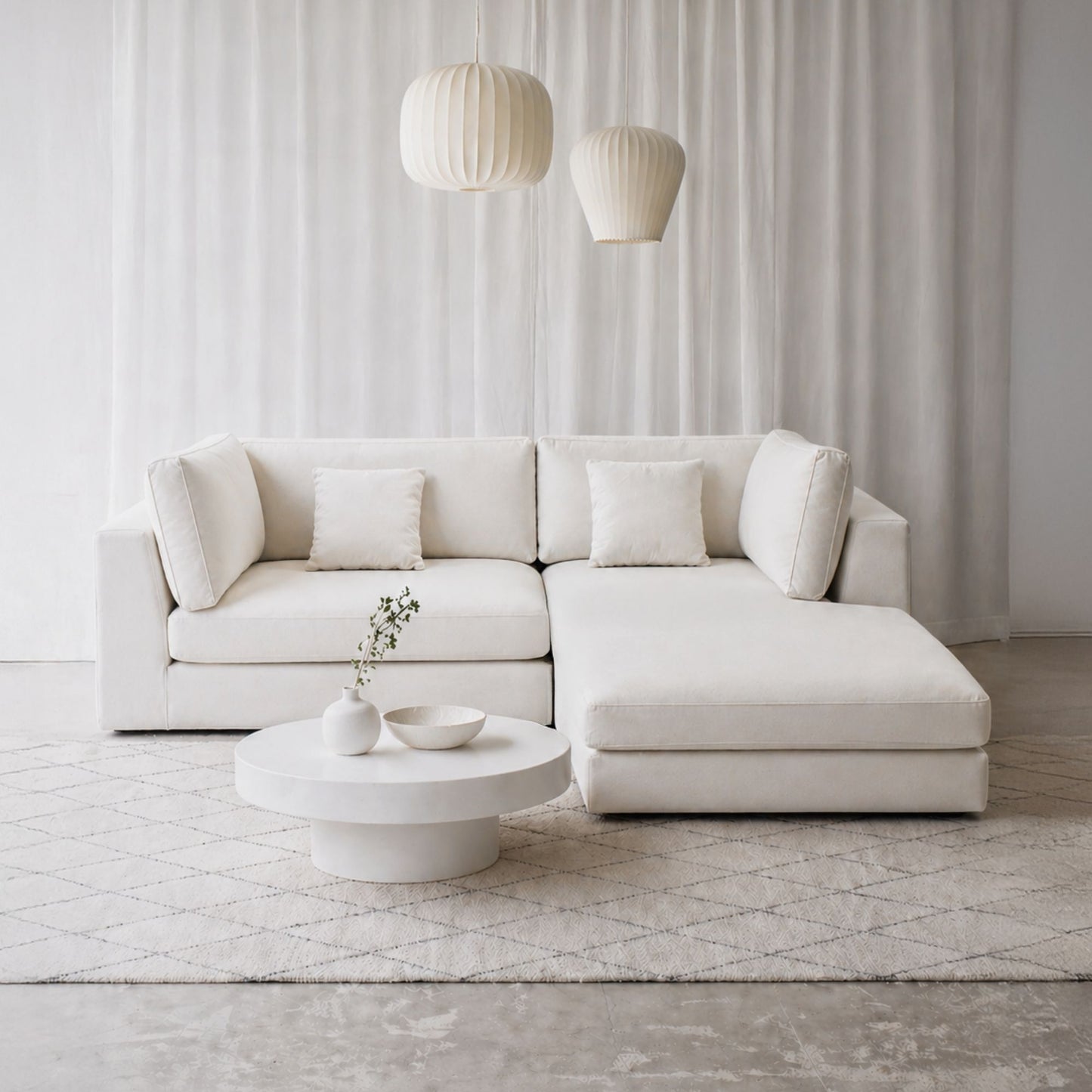 Modern white sectional sofa in a minimalistic living room with a coffee table and decorative items.