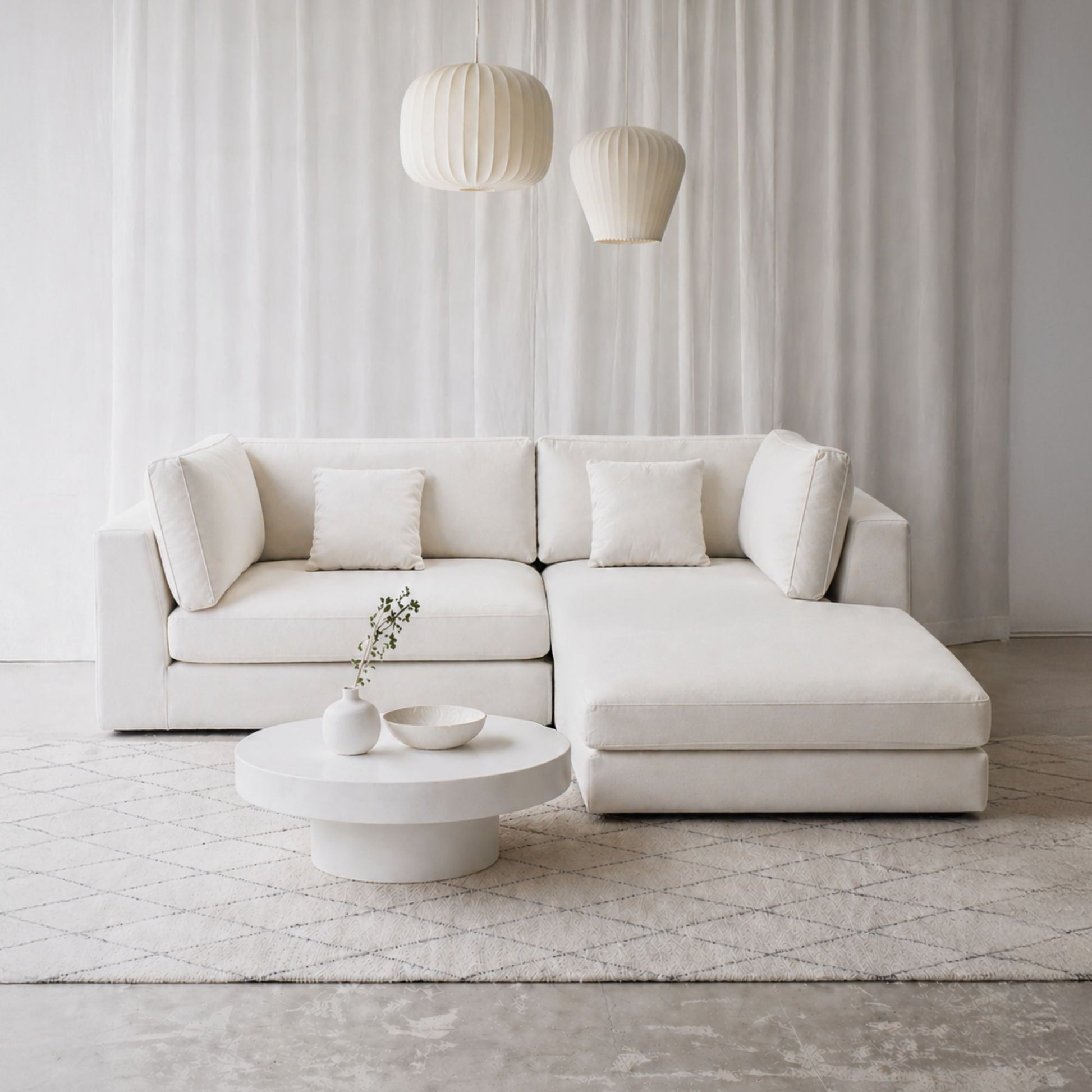 Modern white sectional sofa in a minimalistic living room with a coffee table and decorative items.