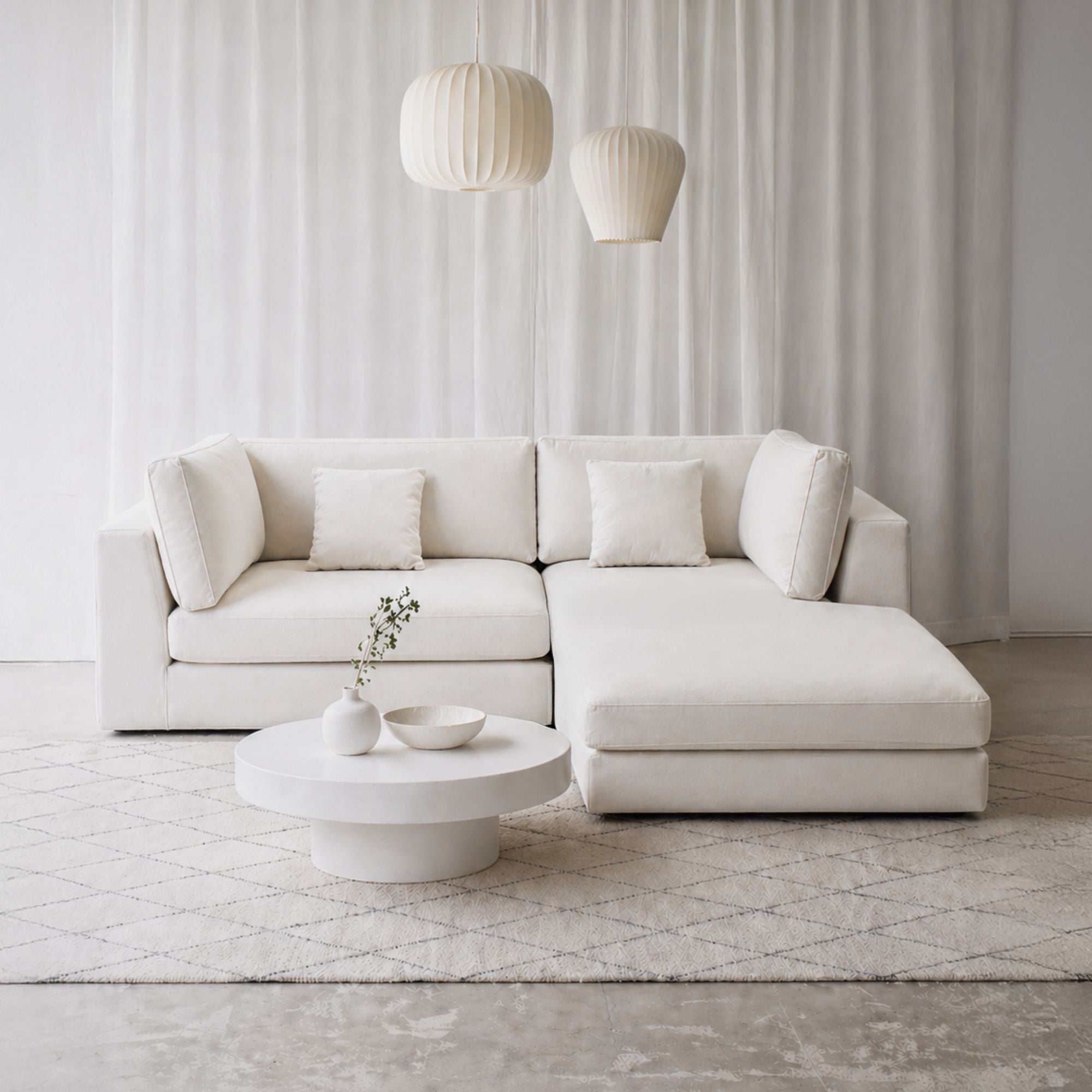 Modern white sectional sofa in a minimalistic living room with a coffee table and decorative items.
