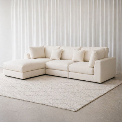White sectional sofa in a minimalistic room with white walls and a rug.