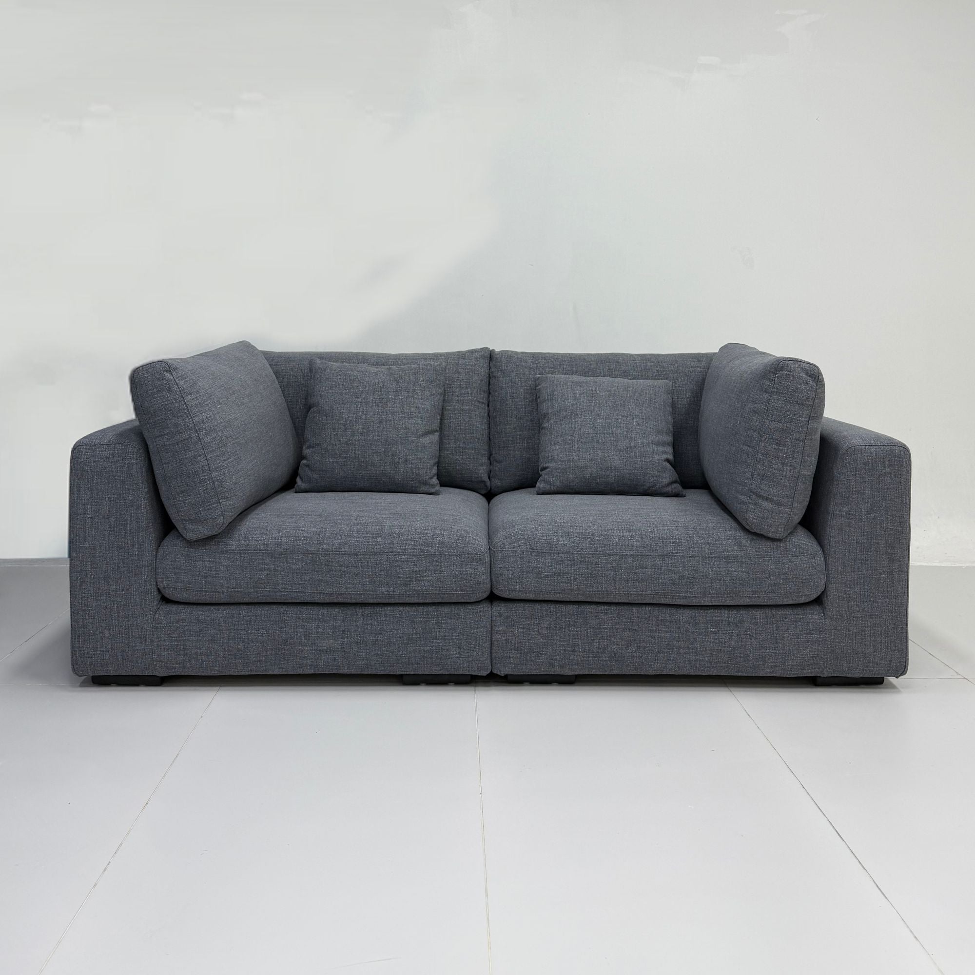 A modern two-seater sofa in textured black fabric with four matching throw pillows, set against a minimalist white studio background.