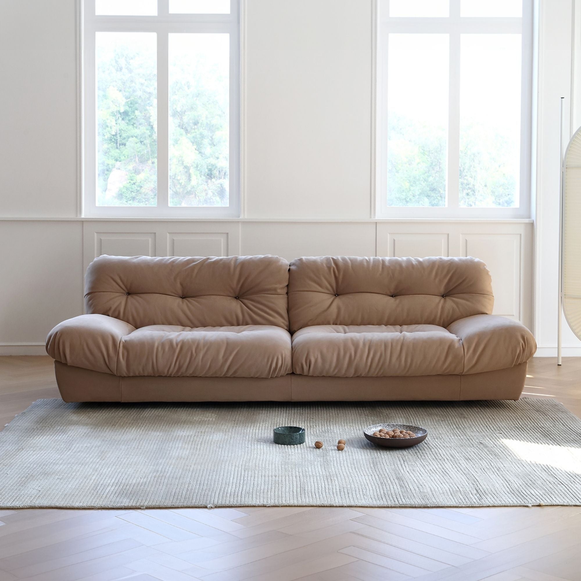 Beige sofa in a room with large windows and a rug.
