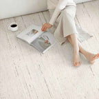 A person sitting barefoot on a light beige textured rug next to an open magazine and a small white cup of coffee in a minimalist indoor setting.