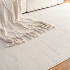 A cream-colored area rug with a subtle textured pattern, styled in a living room setting with a matching cream knit throw blanket draped over a sofa.