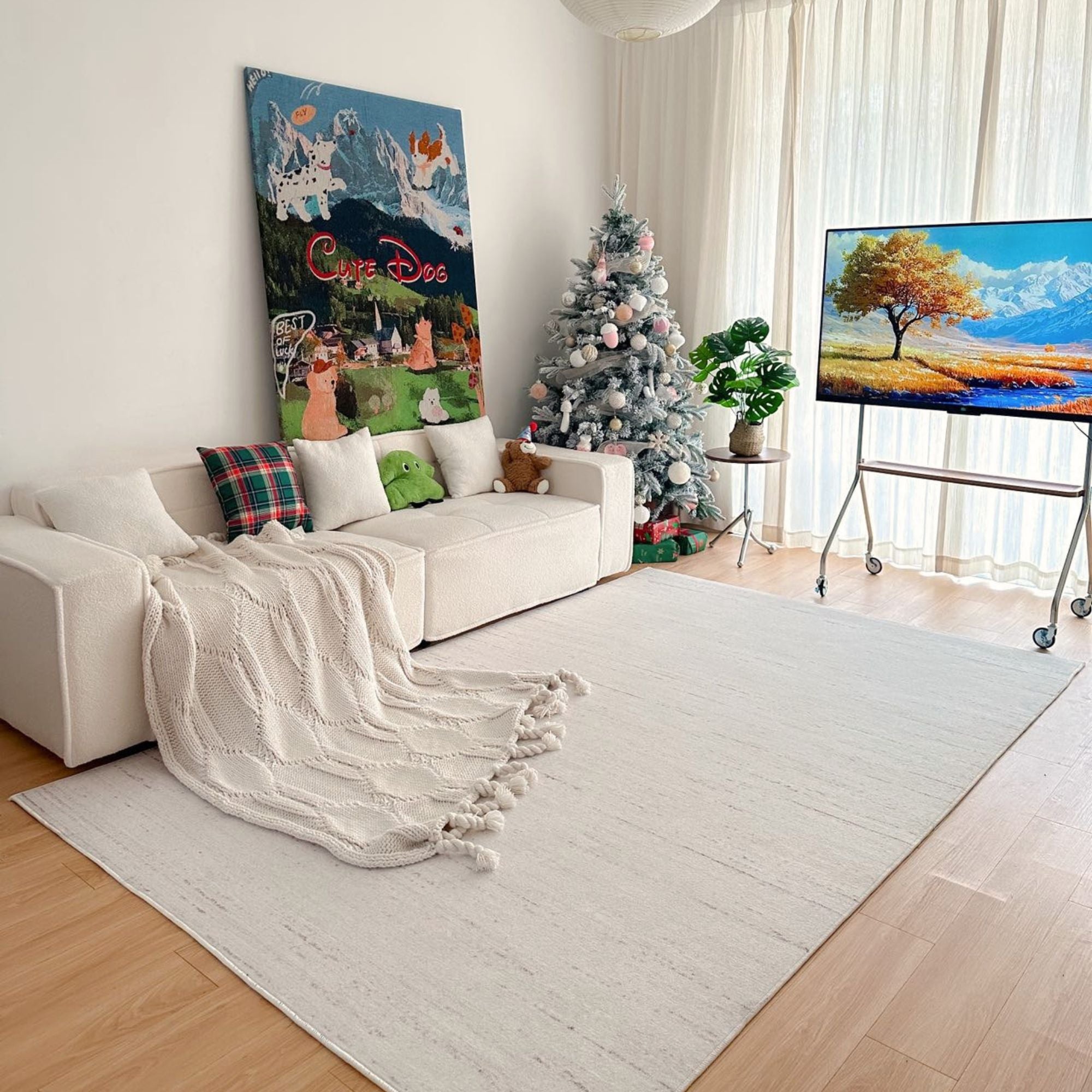 A large off-white area rug with fringe tassels is styled in a bright, modern living room with a white sofa, a decorated Christmas tree, and a TV stand.