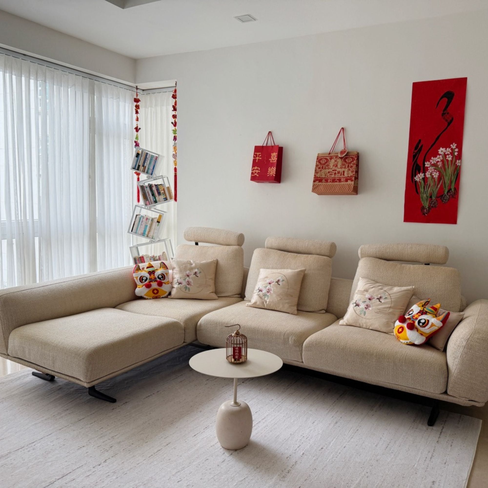 A beige sectional sofa in a bright, modern living room with white walls, a small round coffee table, decorative pillows, and red hanging bags on the wall.