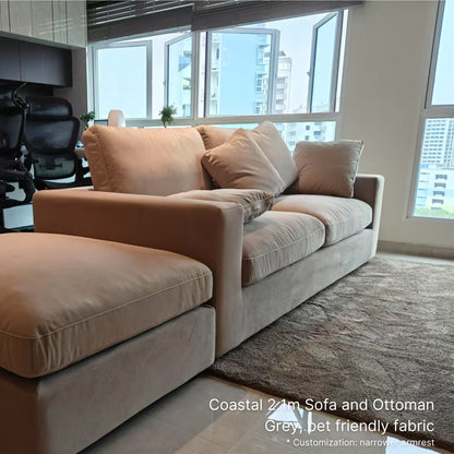Coastal 2.1m Sofa and Ottoman in gray with pet-friendly fabric in a room with large windows.