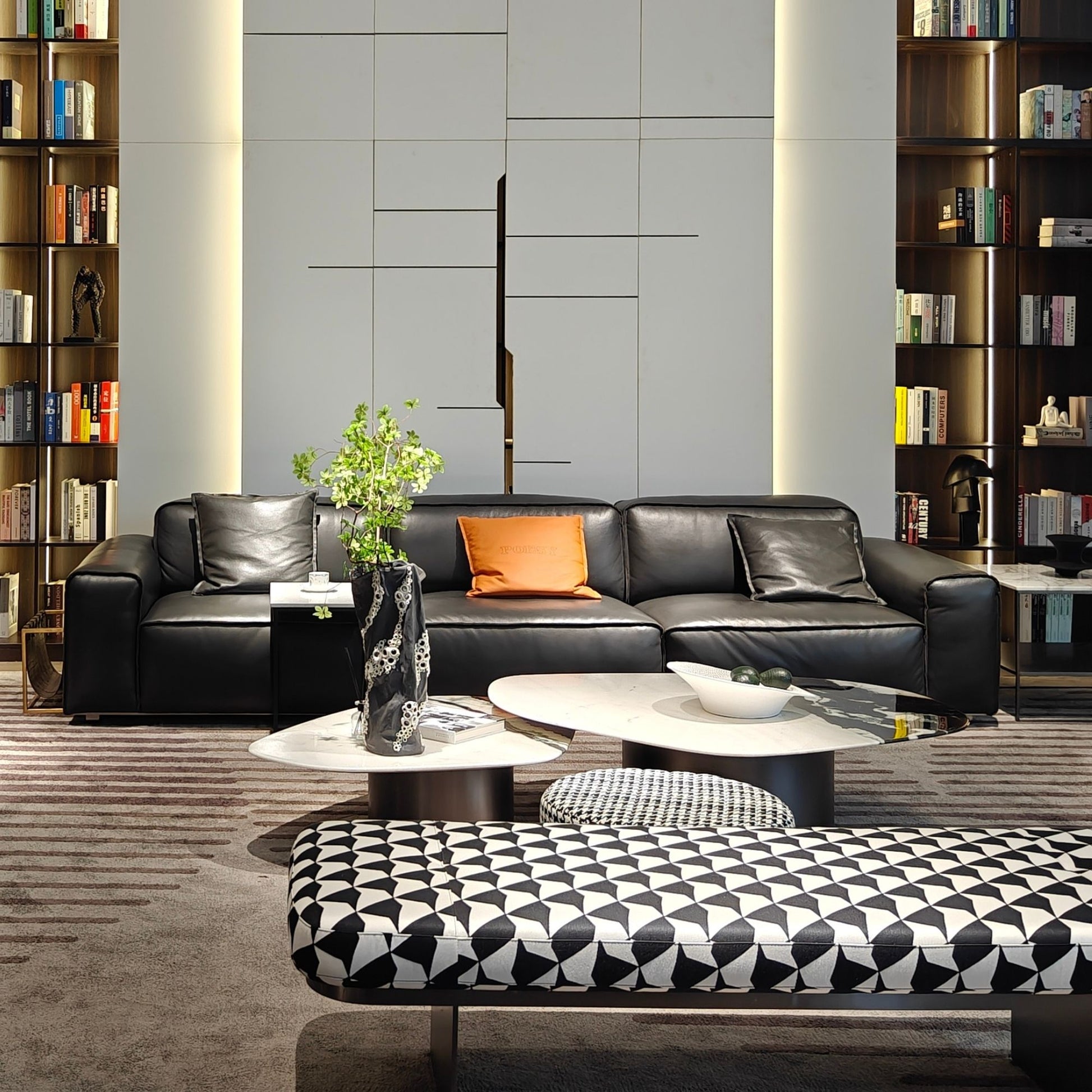 Modern living room with black leather sofa, patterned ottoman, and bookshelves.