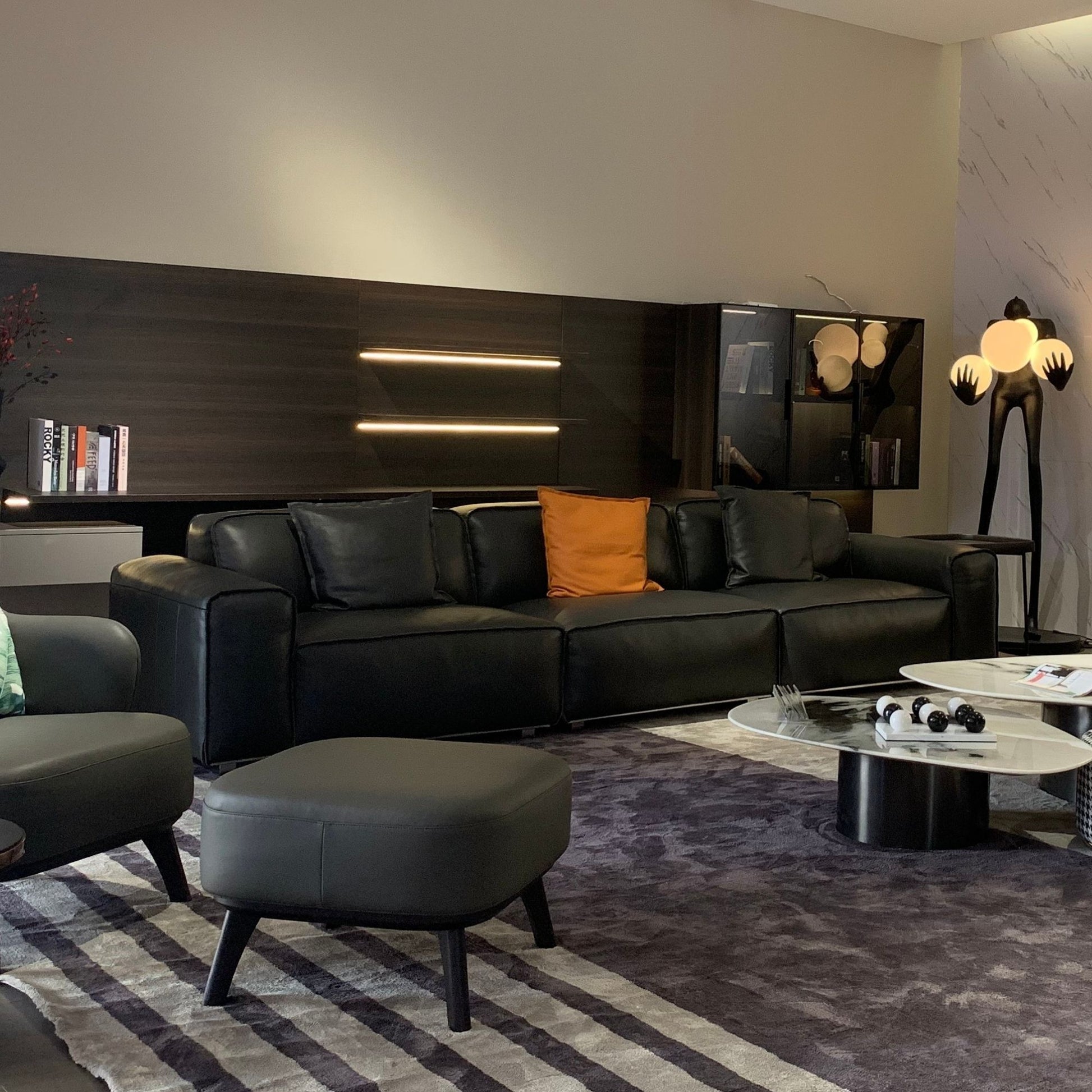 Modern living room with black leather sofa, ottoman, and decorative items.