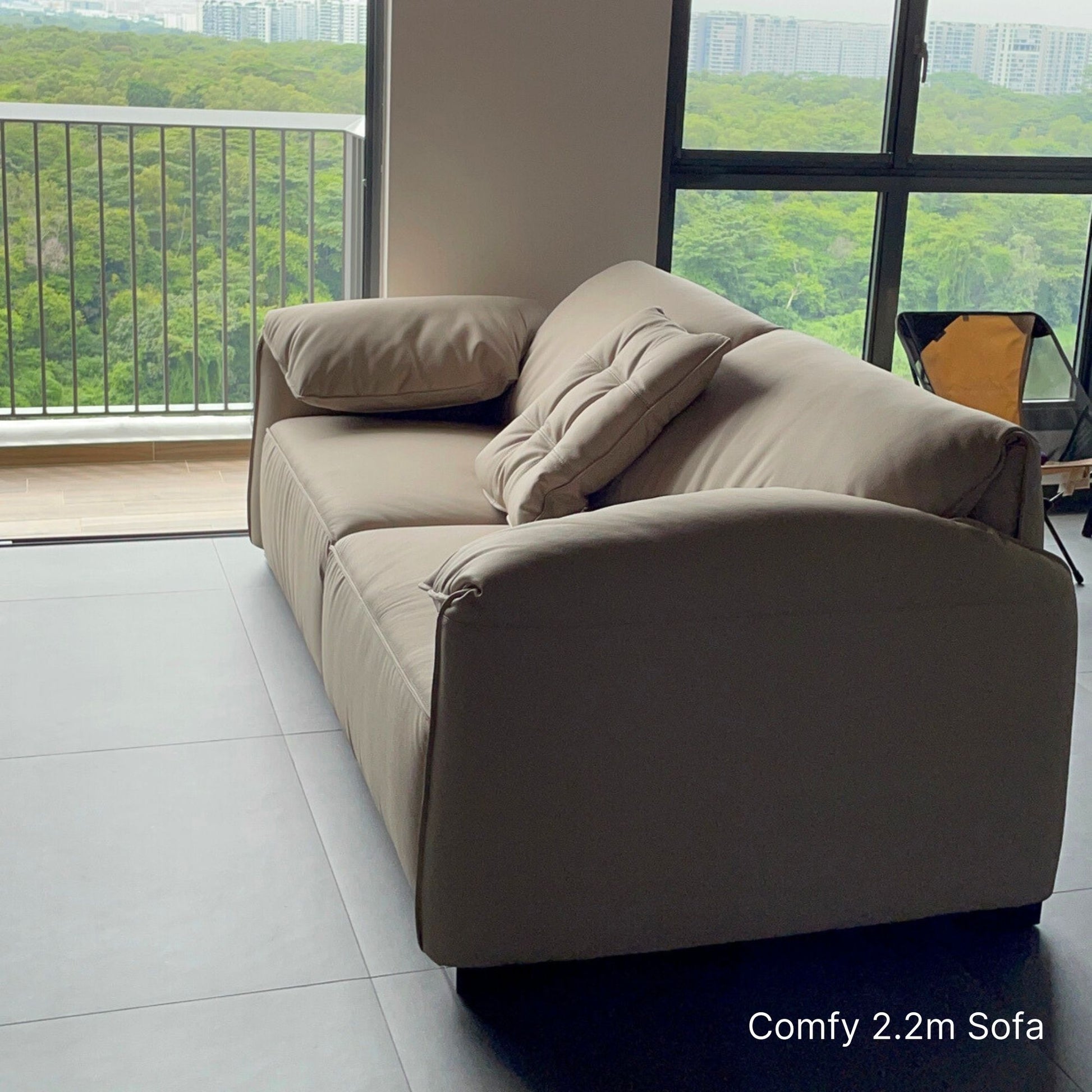 3 seater beige Comfy half leather sofa at 220cm in a modern room with large windows showing greenery outside.