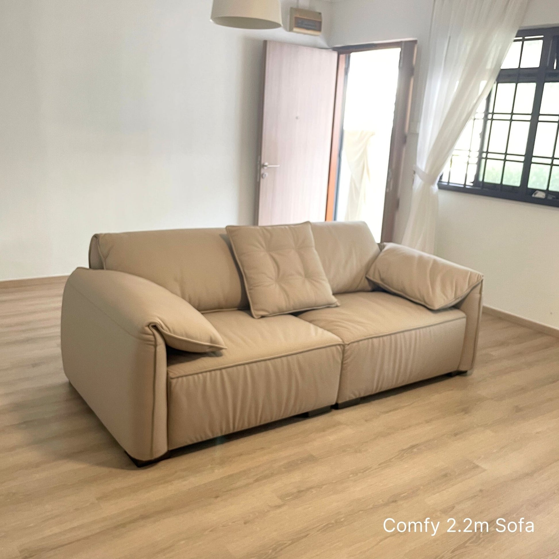 3 seater beige Comfy half leather sofa in a room with wooden flooring and a window.
