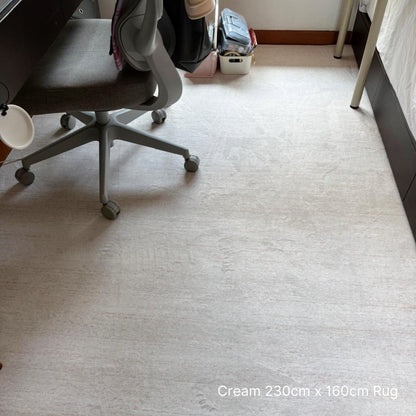 Cream-colored rug on a carpeted floor with furniture and bags in the background