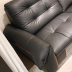 A close-up of a black leather sofa with tufted button details on the backrest and seat, showing the armrest and a small wood accent panel.