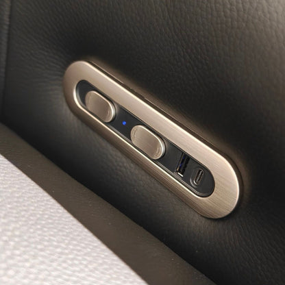 Close-up of a brushed metal control panel with two round buttons and a USB-C port, mounted on a dark textured leather surface.
