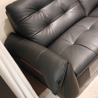 A close-up of a black leather sofa with tufted button details on the backrest and seat, showing the armrest and a small wood accent panel.