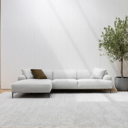 Modern white sectional sofa with a plant in a minimalistic living room.