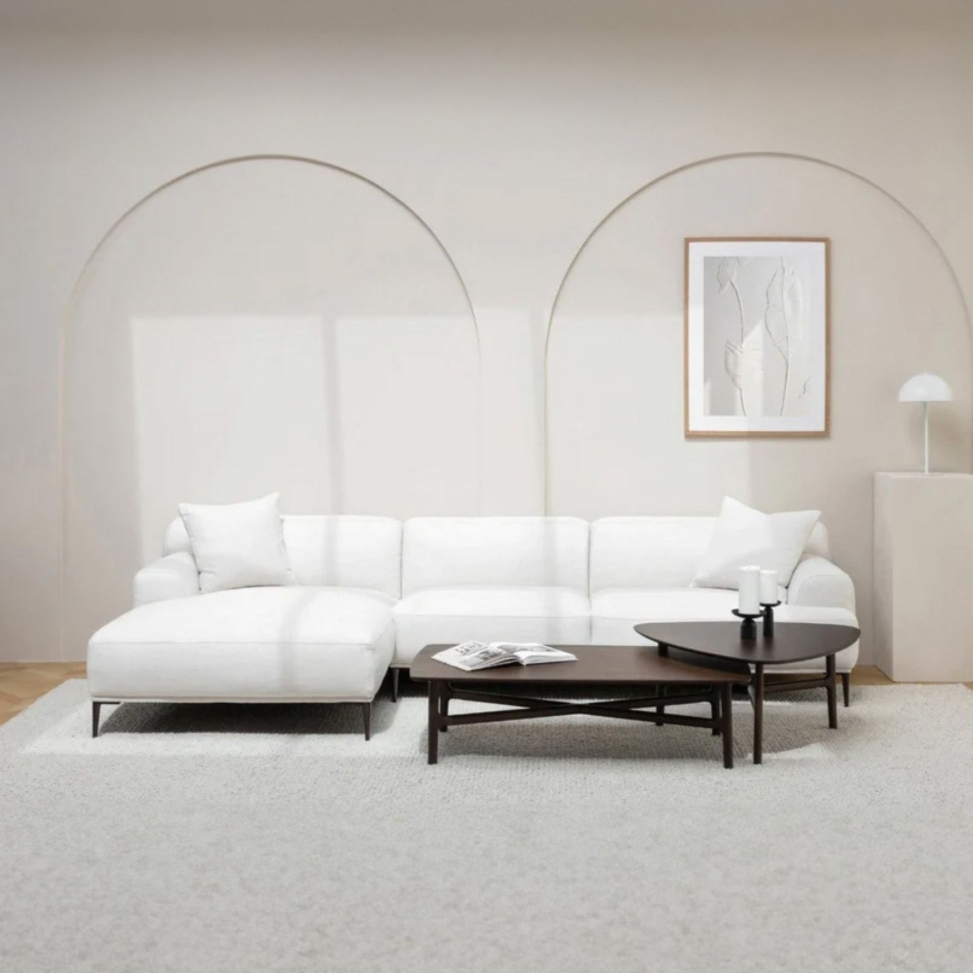 Modern living room with a white L-shapped sectional sofa, coffee table, and abstract art on a light wall.