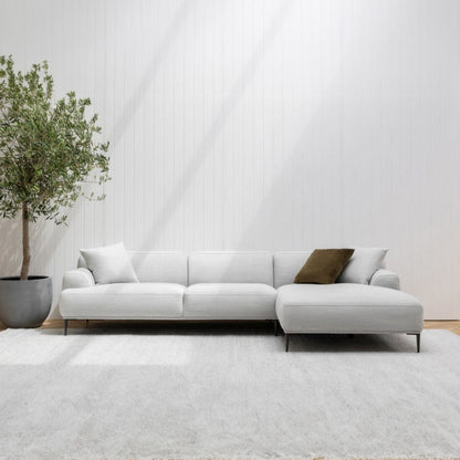 Modern white sectional sofa in a minimalistic living room with a plant and rug.