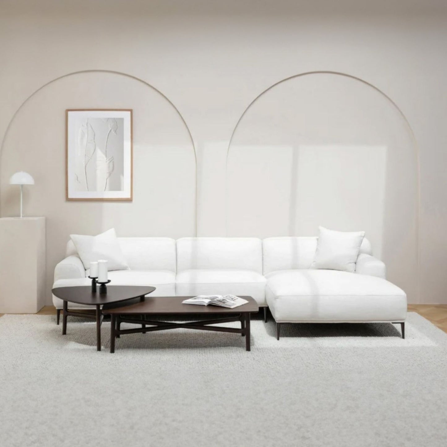 Modern white l-shaped sectional sofa in a minimalistic living room with a coffee table and decorative items.