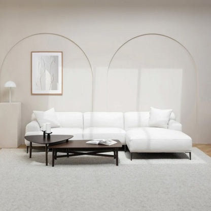 Modern white l-shaped sectional sofa in a minimalistic living room with a coffee table and decorative items.