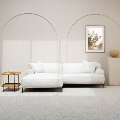 Modern living room with a white l-shaped sofa, small table, and framed artwork on a neutral wall.