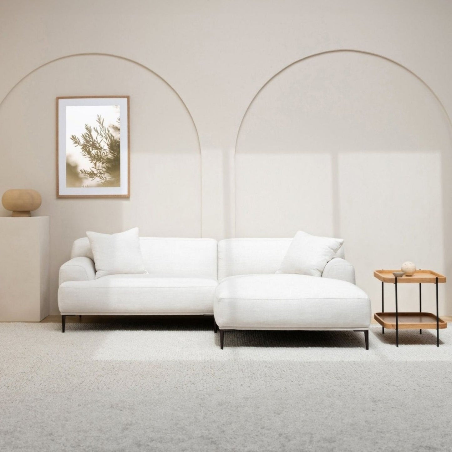 Modern white l-shaped sectional sofa in a minimalistic living room with a small table and framed picture.