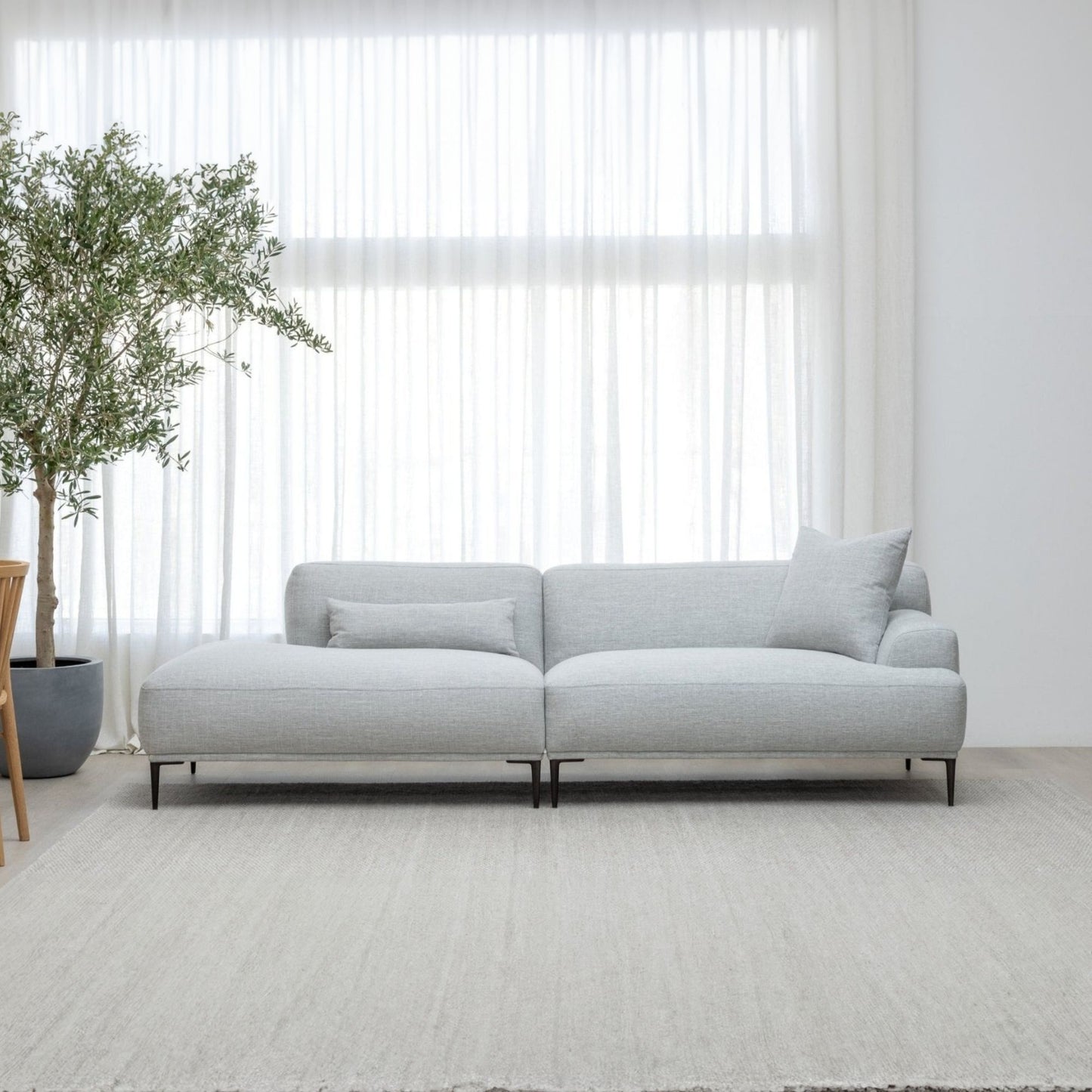 Gray sectional sofa in a minimalistic room with a plant and large window.