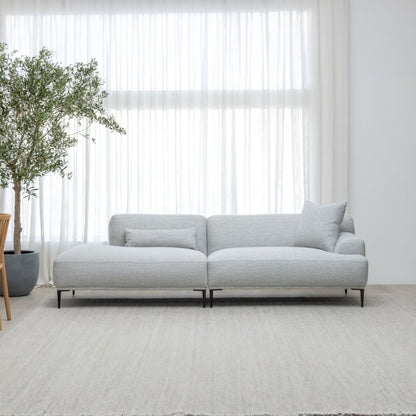 Gray sectional sofa in a minimalistic room with a plant and large window.
