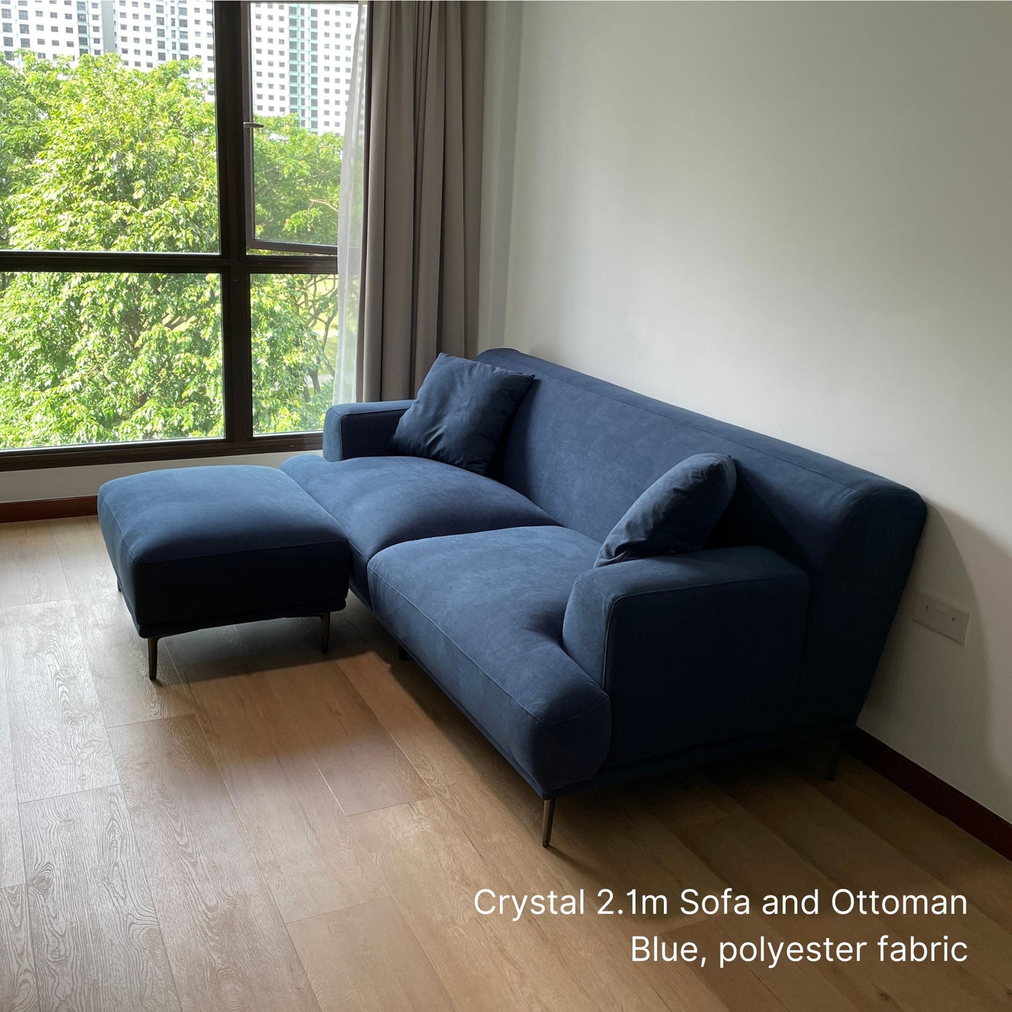 Crystal 3 seater blue fabric sofa and ottoman in a room with large windows and greenery outside