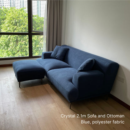 Crystal 3 seater blue fabric sofa and ottoman in a room with large windows and greenery outside
