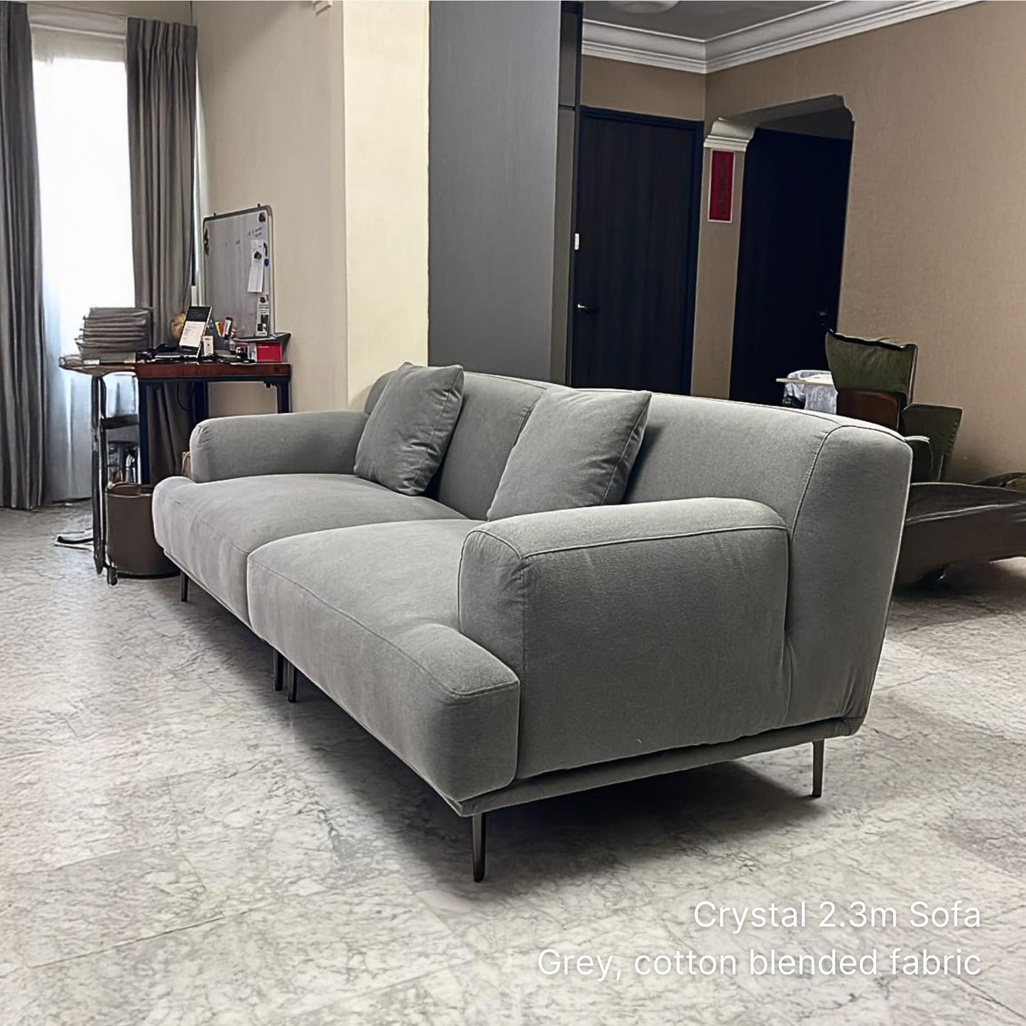 3 seater gray cotton blended fabric sofa in a room with a desk and curtains.