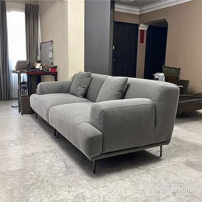 3 seater gray cotton blended fabric sofa in a room with a desk and curtains.