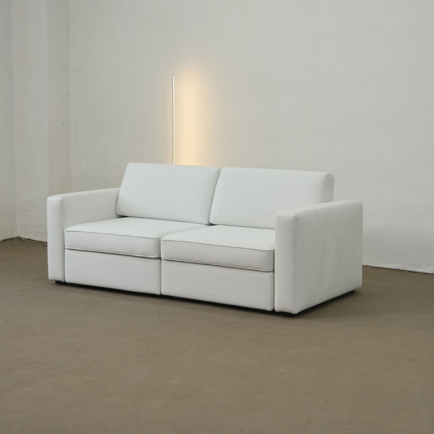 White sofa in a minimalistic room with a lamp on a white wall.