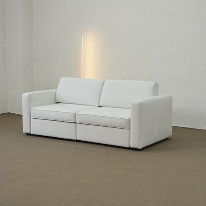 White sofa in a minimalistic room with a lamp on a white wall.