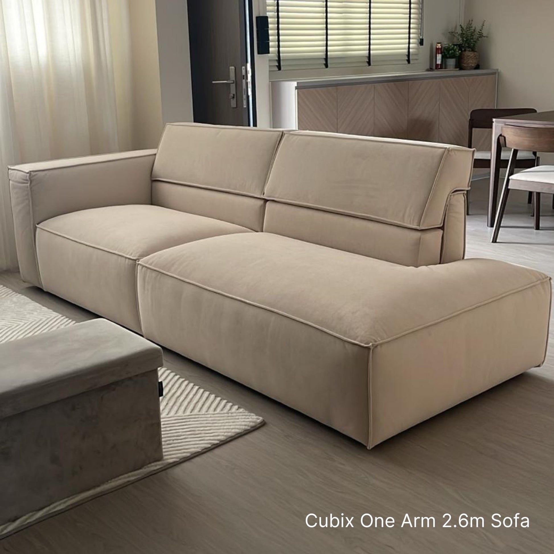 Beige sectional sofa in a living room setting with a dining area in the background.