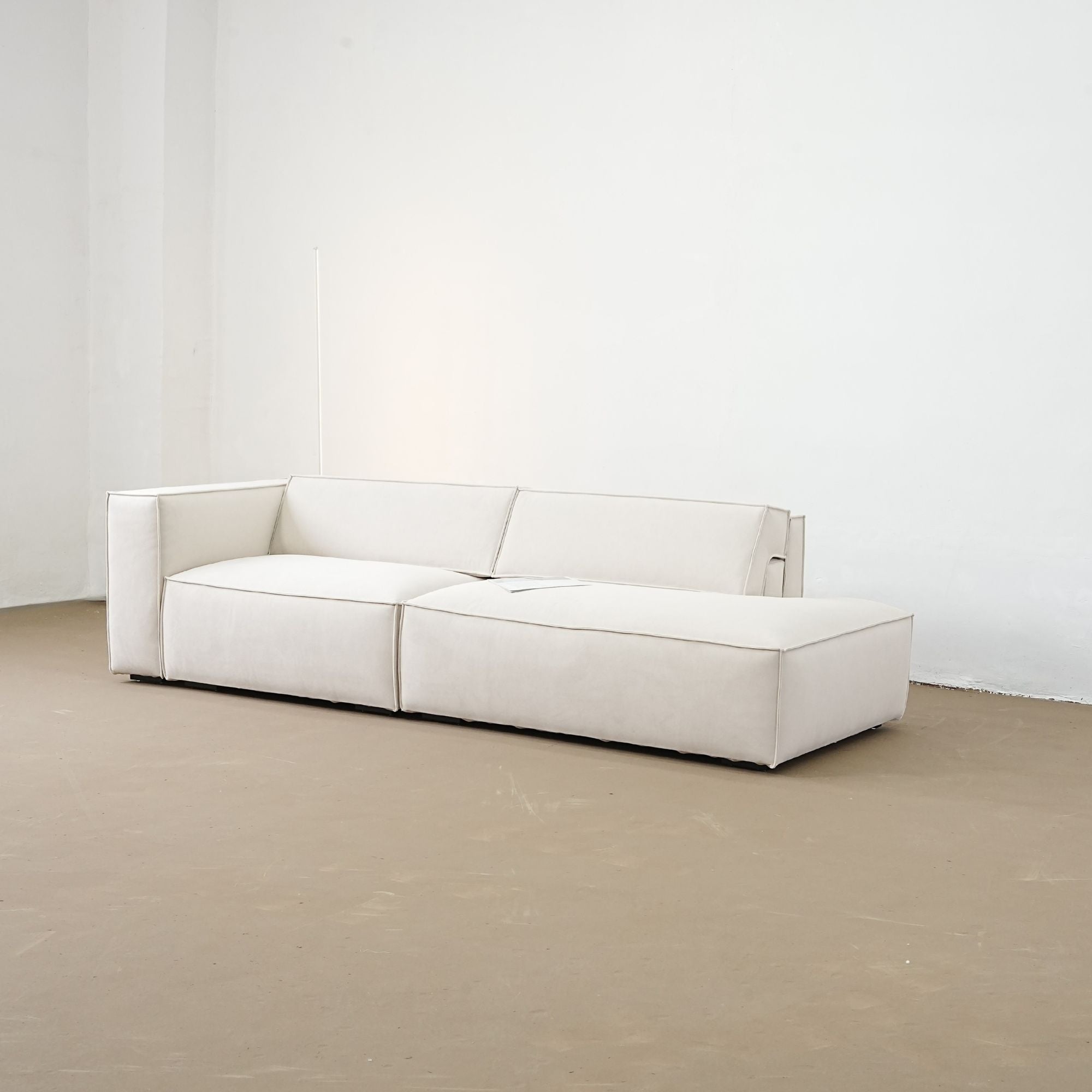White sofa in a minimalistic room with white walls and a beige floor.
