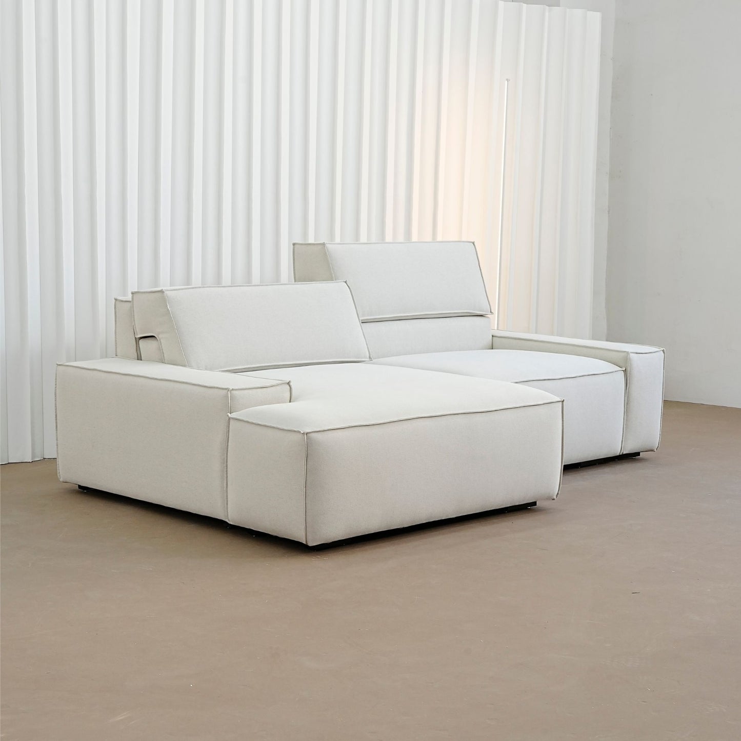 White modular sofa in a minimalistic room with white curtains.