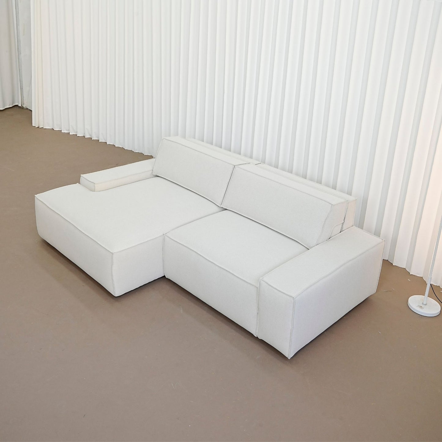 Beige sectional sofa in a minimalistic room with white walls and a brown floor.