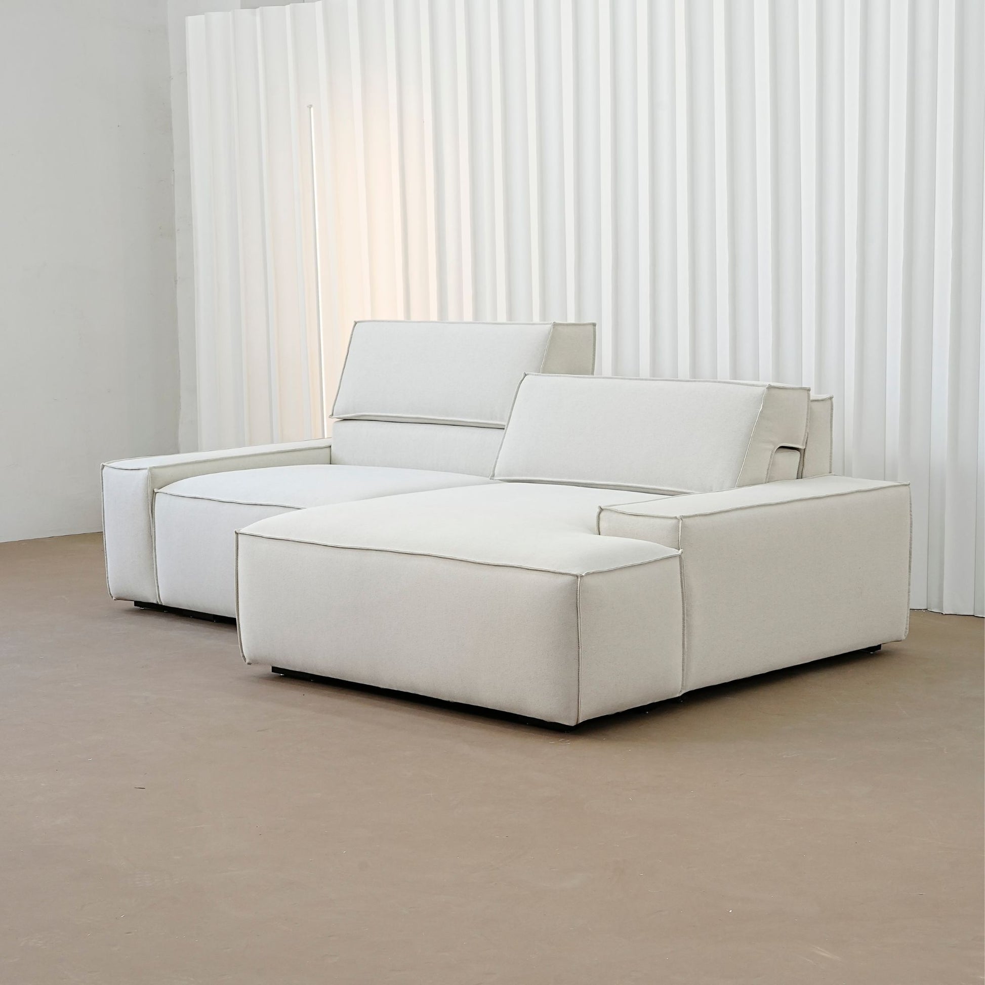 Beige sectional sofa in a minimalistic room with white curtains.